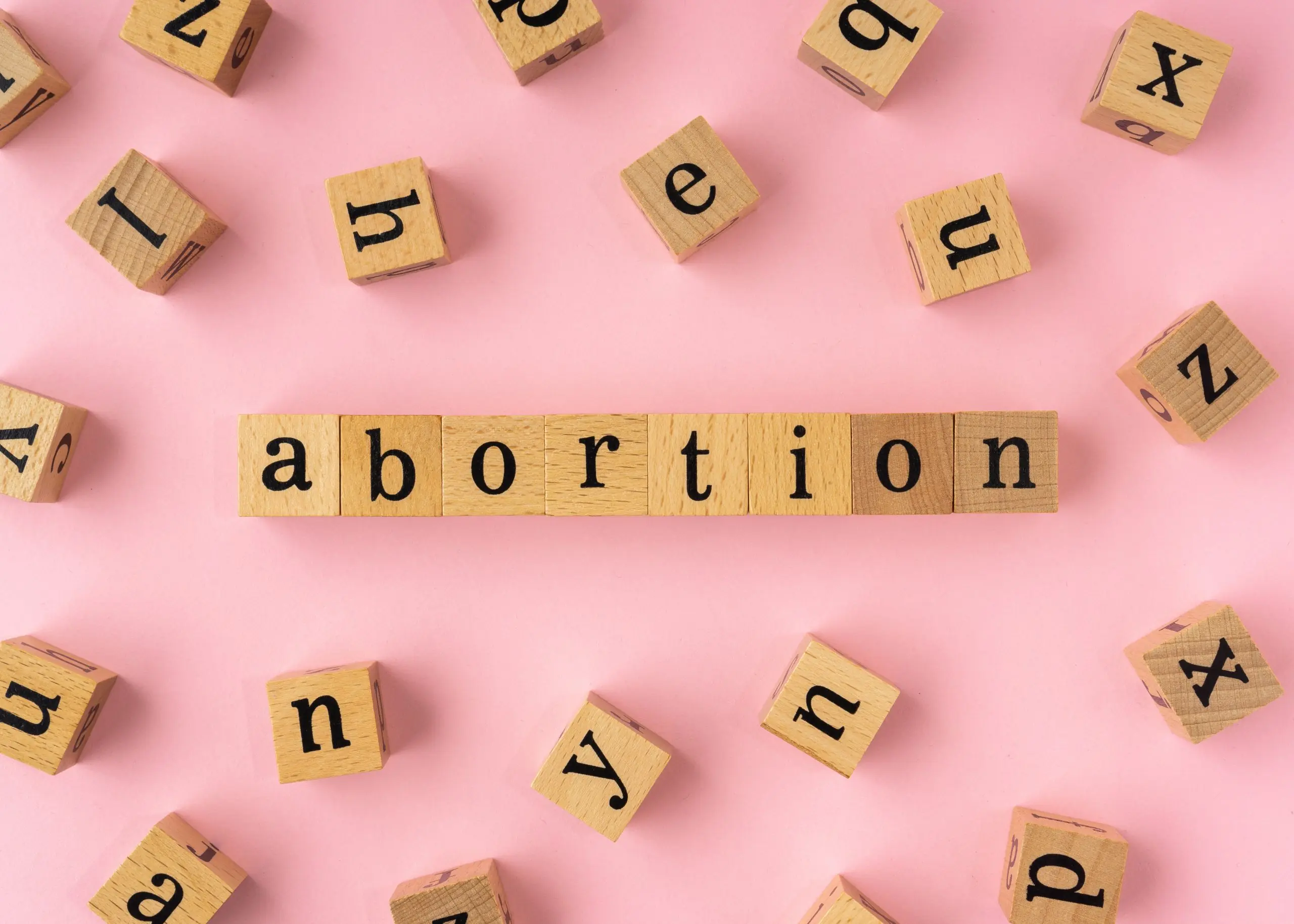 Abortion word on wooden block. Flat lay view on light pink background.